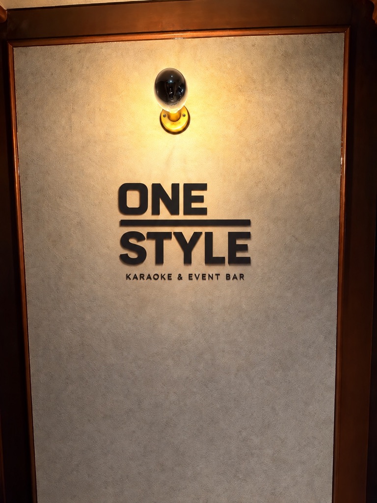 温かな照明と木枠に囲まれた壁面のONE STYLEロゴ